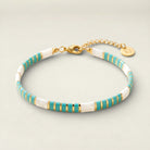 Bracelet with turquoise, gold, and white stripes on a beige background