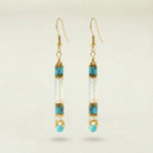 Pair of gold earrings with turquoise and clear beads on a beige background