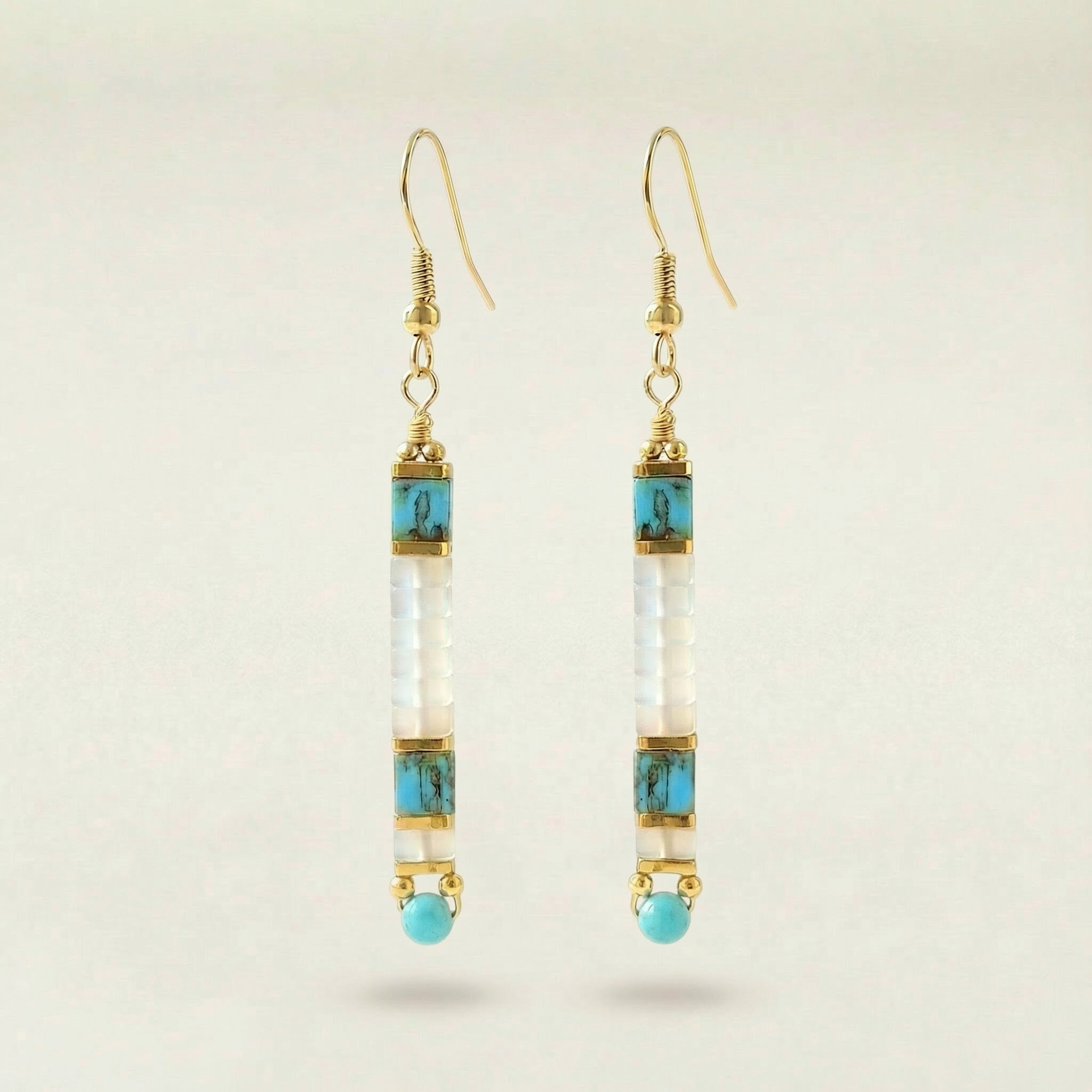 Pair of gold earrings with turquoise and clear beads on a beige background