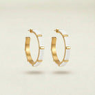 Gold hoop earrings with white ceramic accents on a beige background