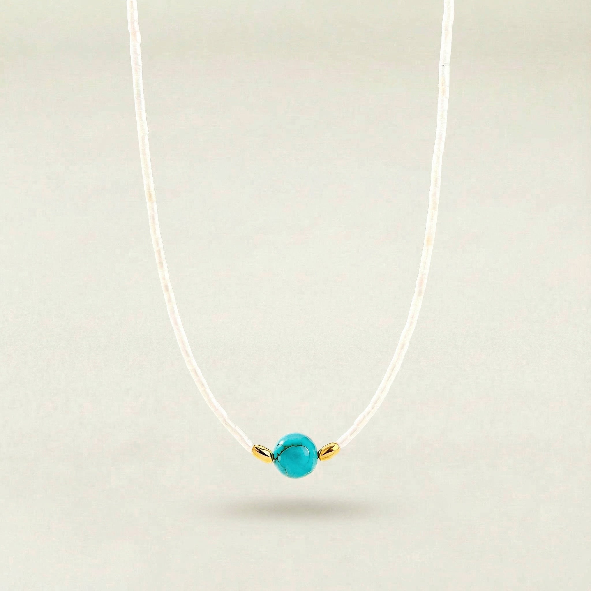 Necklace with a turquoise bead and gold accent on a light gray background
