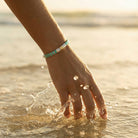 Hand with a bracelet touching water at sunset