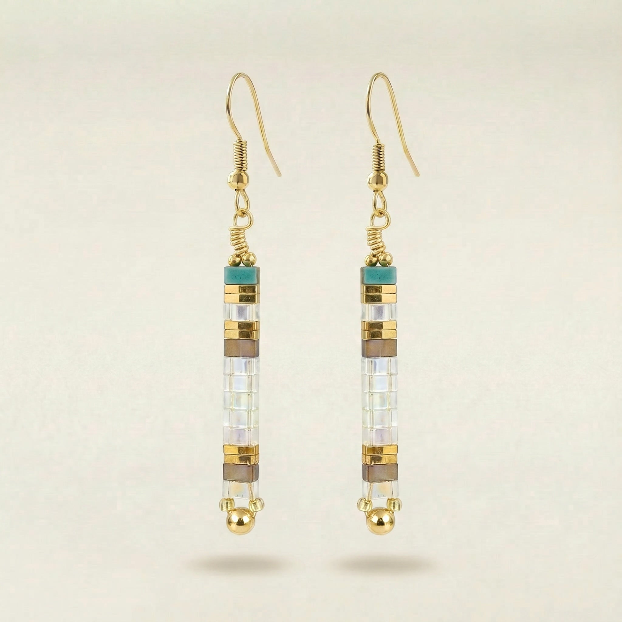 Gold earrings with cylindrical beads on a beige background